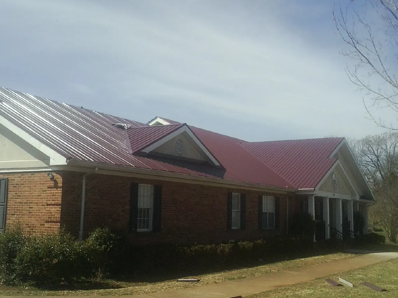Red metal roof with gabled entries on a long brick building, from a Hail Damage Roof Repair job in Desert Hot Springs