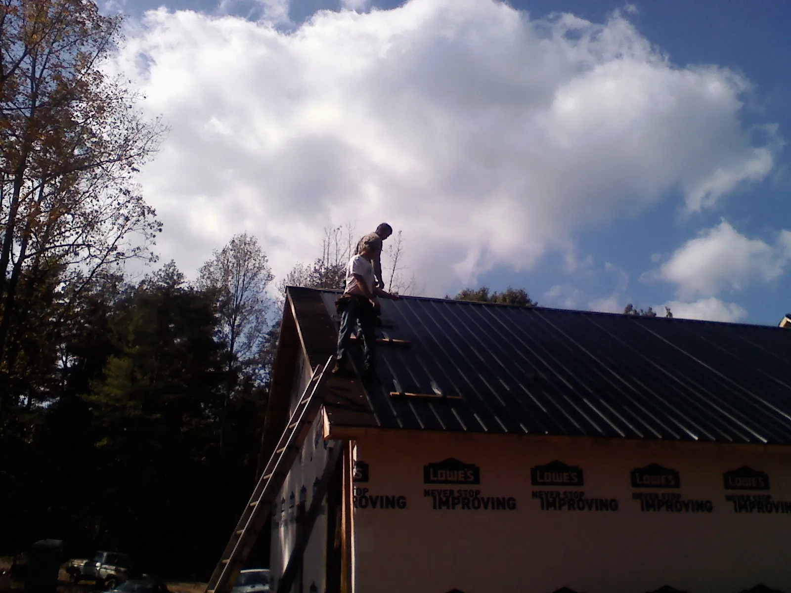Roofer fastening dark metal panels high against a cloudy sky, from a Roof Inspection job in Desert Hot Springs