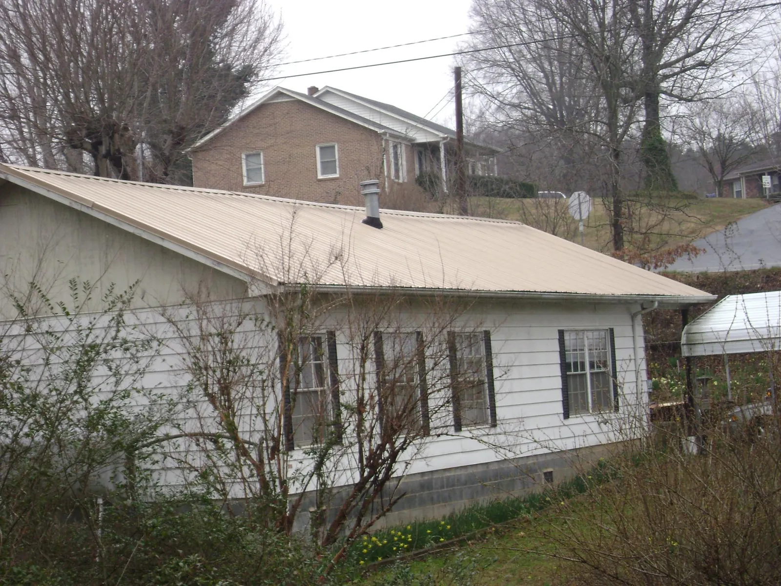 Tan metal roof on a white sided house set into a hillside — Commercial Roofing by Roofing Brothers in Desert Hot Springs