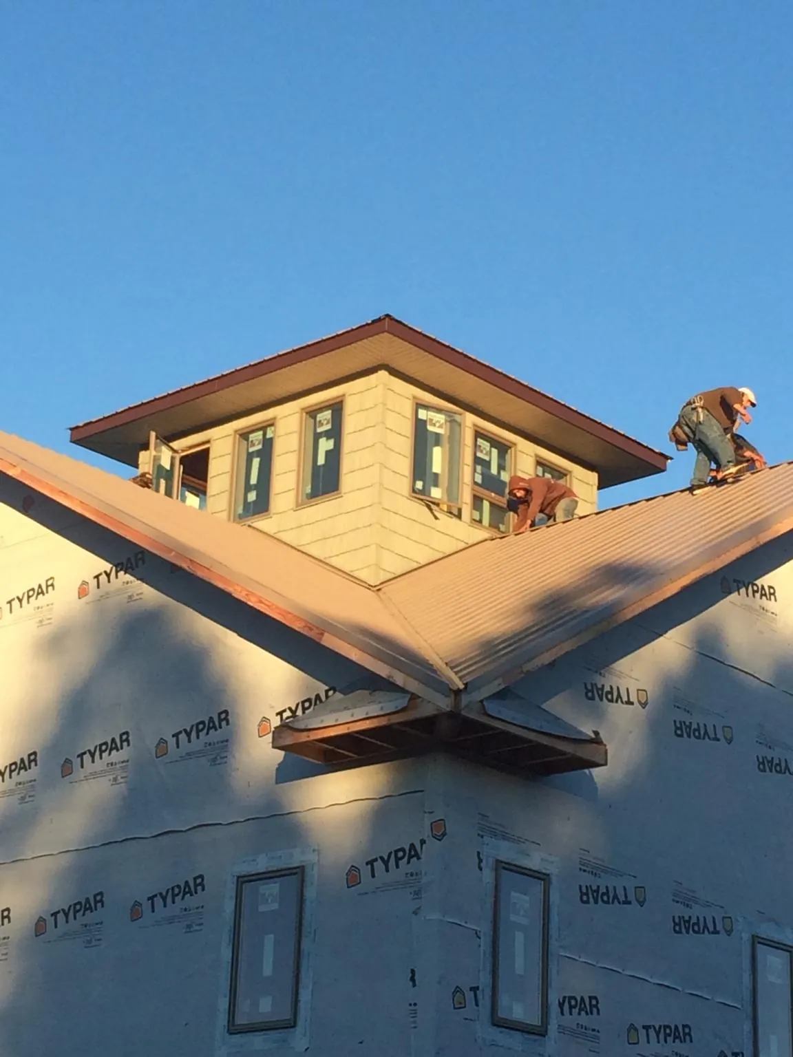 Roofers working around a rooftop cupola on a new metal roof at sunset — Roof Waterproofing in Desert Hot Springs by Roofing Brothers
